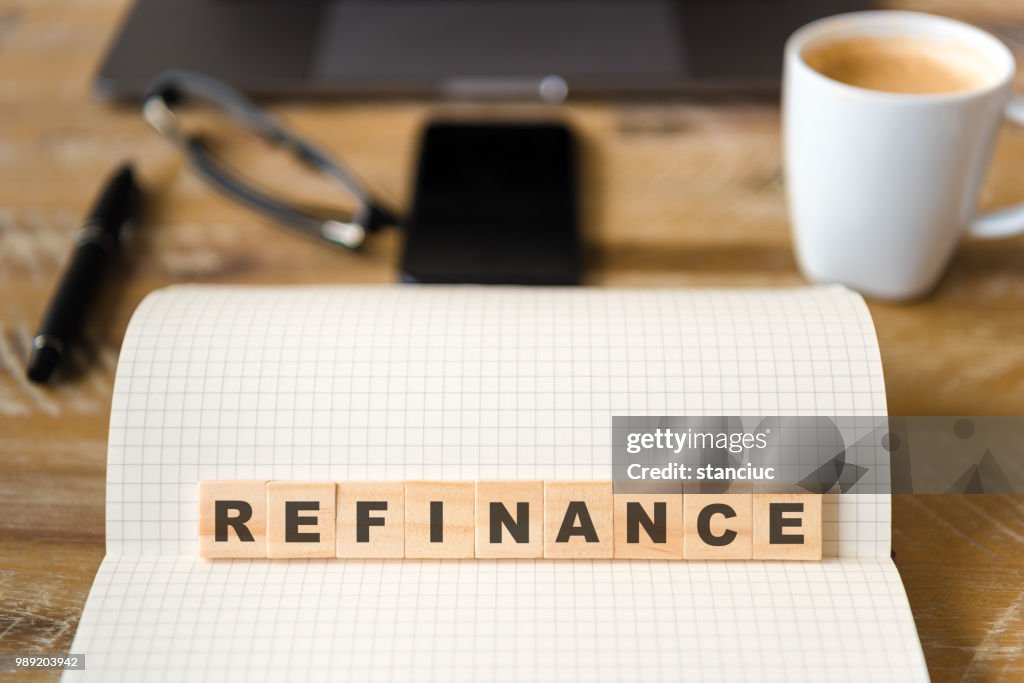 Closeup on notebook over wood table background, focus on wooden blocks with letters making Refinance text
