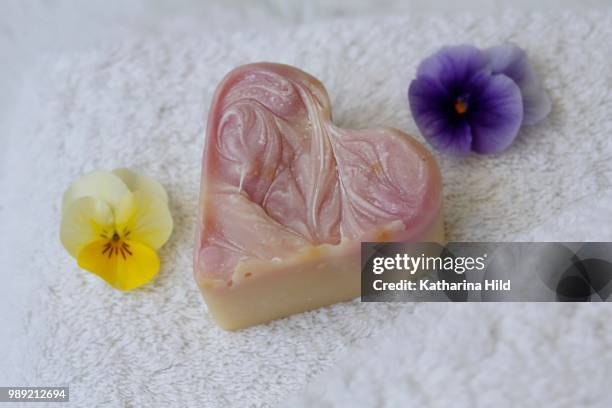 soap in heart shape on terry towel with flowers of horned violets - katharina herz stock-fotos und bilder