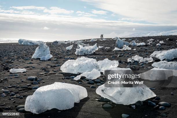 two tourists walking at horizon, ice floes on black beach, diamond beach, fjallsarlon glacier lagoon, east iceland, iceland - austurland stock pictures, royalty-free photos & images