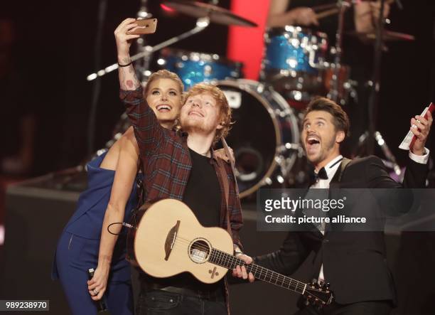 Presenters Lena Gercke and Thore Schoelermann stand onstage with musican Ed Sheeran during the finale of the ProSiebenSat.1 show "The Voice of...