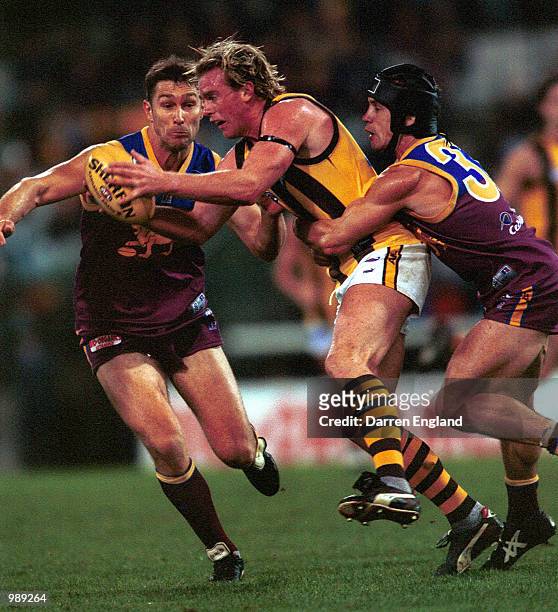 Rayden Tallis of Hawthorn is tackled by Alastair Lynch and Shaun Hart of Brisbane during the round 13 AFL match between the Brisbane Lions and the...