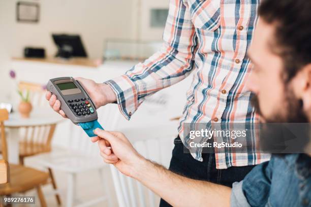 young man in a coffee shop putting his credit card in a credit card reader - earring card stock pictures, royalty-free photos & images