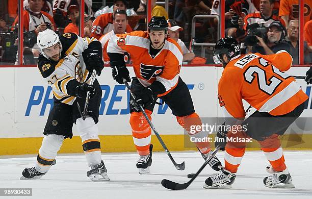 Patrice Bergeron of the Boston Bruins skates against Ville Leino and Daniel Carcillo of the Philadelphia Flyers in Game Three of the Eastern...