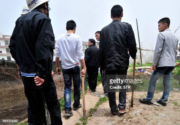 Chinese authorities carry sticks as they stand guard while workers demolish houses which are claimed illegal by local government in Wuhan, central...