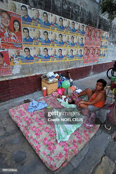 Mother with her child live beside a wall plastered with election campaign posters featuring local politicians in Manila on May 9, 2010. More than...