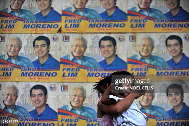 Child carries her baby brother near a wall full of election campaign posters of local politicians in Manila on May 9, 2010. More than 17,000...