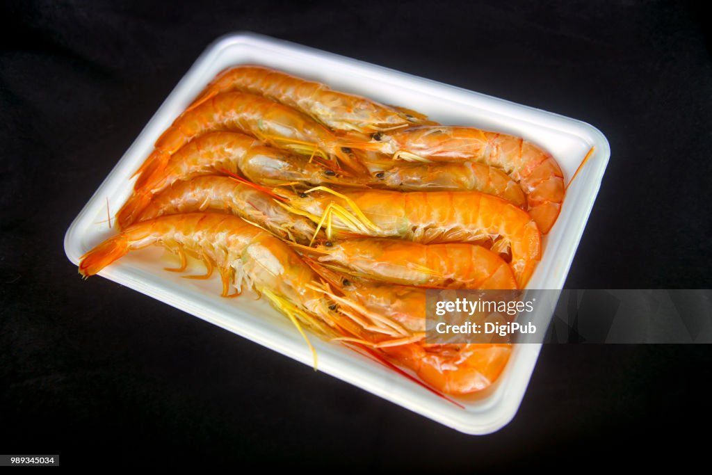 Argentine red shrimp, ten in white plastic tray on black background
