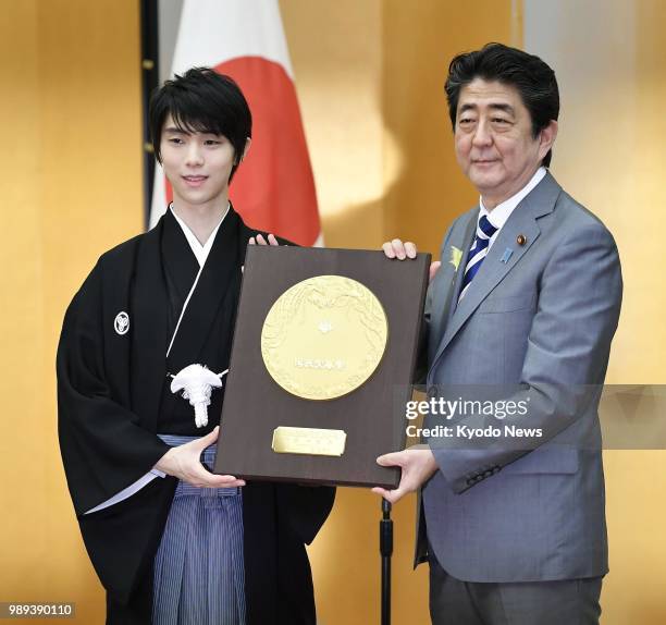 Two-time figure skating Olympic gold medalist Yuzuru Hanyu poses for photos with Japanese Prime Minister Shinzo Abe as he receives the People's Honor...