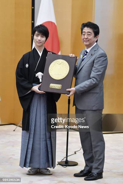 Two-time figure skating Olympic gold medalist Yuzuru Hanyu poses for photos with Japanese Prime Minister Shinzo Abe as he receives the People's Honor...