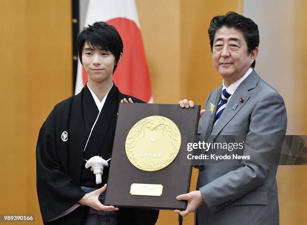 Two-time figure skating Olympic gold medalist Yuzuru Hanyu poses for photos with Japanese Prime Minister Shinzo Abe as he receives the People's Honor...