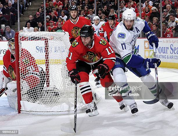 John Madden of the Chicago Blackhawks and Ryan Kesler of the Vancouver Canucks skate behind the net, protected by Blackhawks goalie Antti Niemi, as...