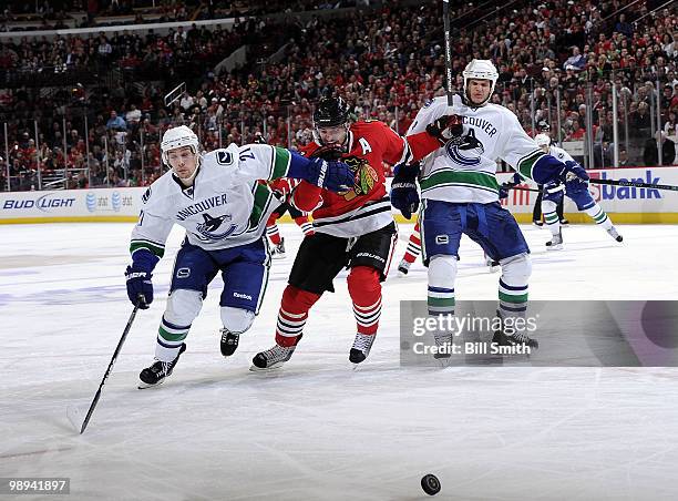 Patrick Sharp of the Chicago Blackhawks skates in between Mason Raymond and Kevin Bieksa of the Vancouver Canucks, as they chase after the puck, at...