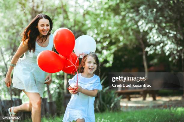 giovane donna con bambino in abito bianco con palloncini colorati all'aperto - mamma bambina palloncino bianco foto e immagini stock