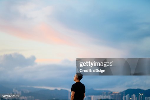 Young man enjoying the tranquility while gazing at dramatic sky in deep thought Young man enjoying the tranquility while gazing at dramatic sky in deep thought