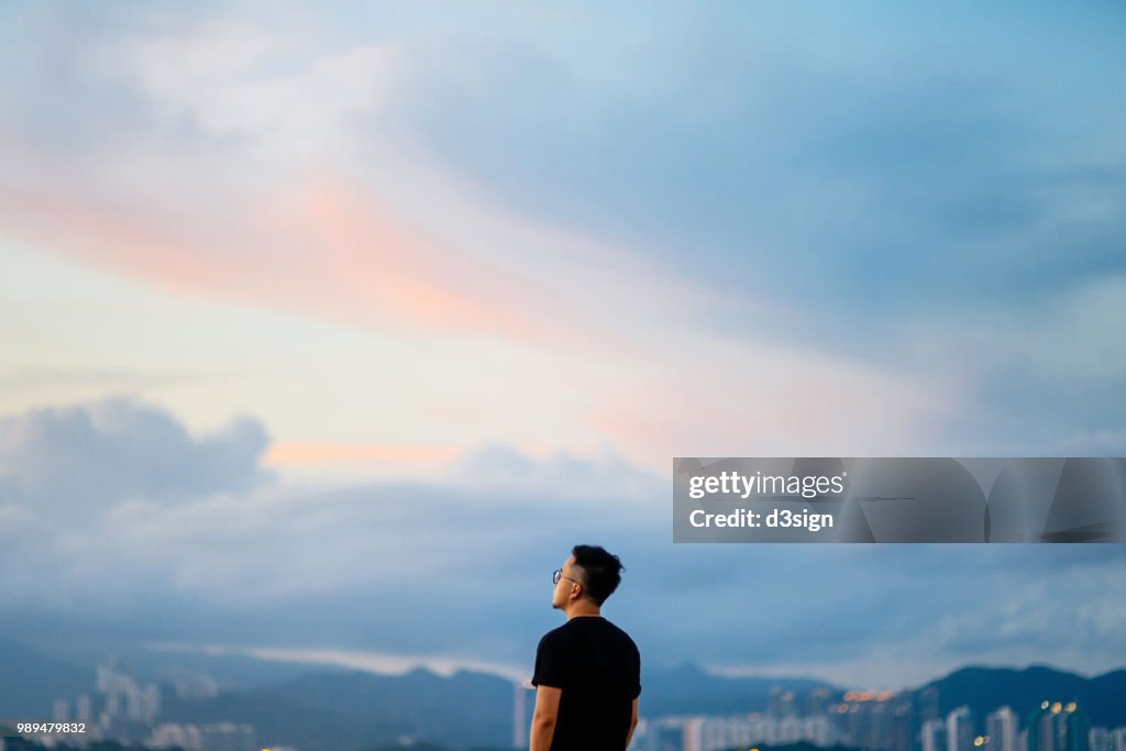Young man enjoying the tranquility while gazing at dramatic sky in deep thought