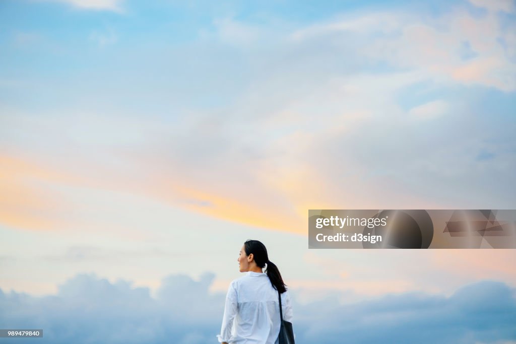 Beautiful young woman enjoying the fresh air and gentle wind breeze against beautiful sky