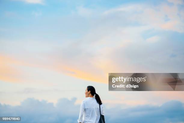 beautiful young woman enjoying the fresh air and gentle wind breeze against beautiful sky - windy city stock pictures, royalty-free photos & images