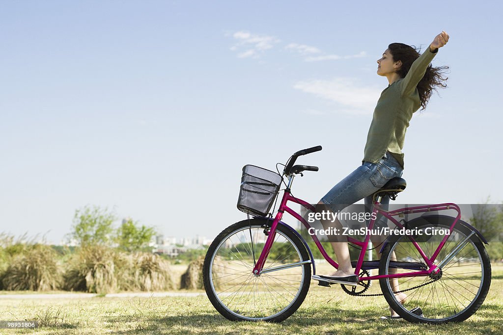 Young woman sitting on bicycle with arms out and eyes closed