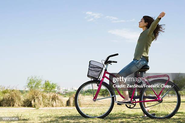 young woman sitting on bicycle with arms out and eyes closed - hands free cycling stock pictures, royalty-free photos & images