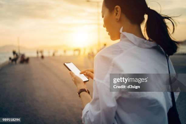 young lady using smartphone while having a relaxing walk by the pier afterwork at sunset - young people mobile free stock pictures, royalty-free photos & images