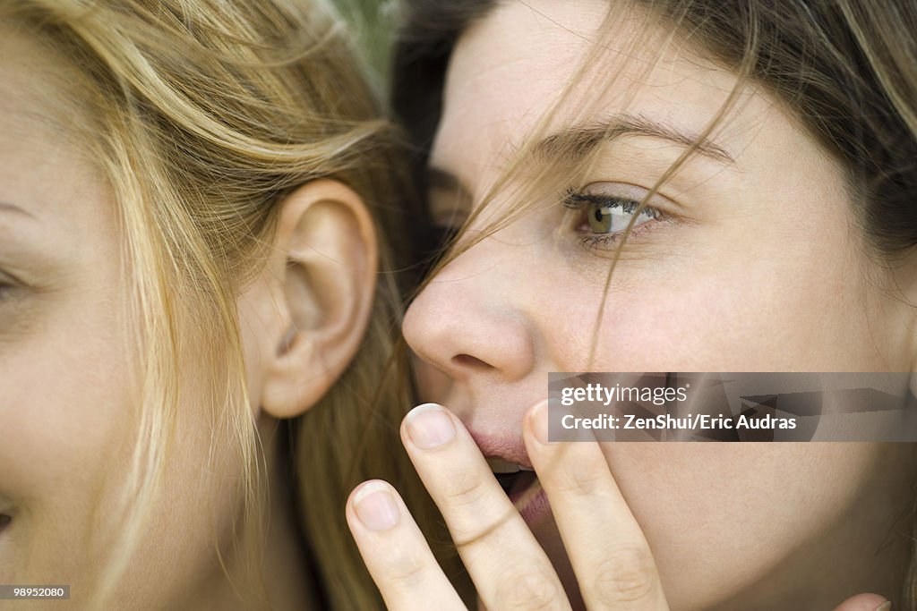 Young woman whispering secret into friend's ear, close-up