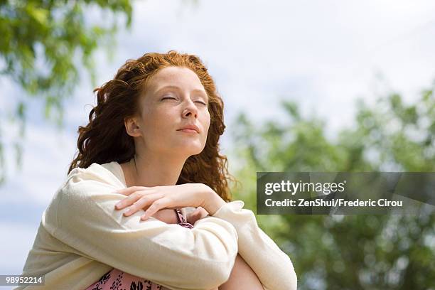 young woman sitting outdoors with eyes closed - beeldtechniek stockfoto's en -beelden