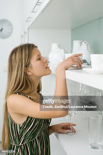 young woman looking for dish stored on shelf - opbergen stockfoto's en -beelden