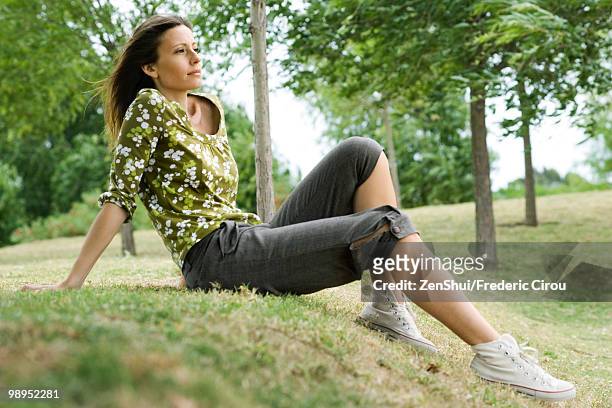 woman sitting on grass in park, looking away in thought - leaning tree stock pictures, royalty-free photos & images