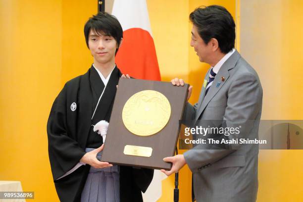 Two-time Olympic figure skating Men's Singles gold medalist Yuzuru Hanyu receives the plaque from Japanese Prime Minister Shinzo Abe during the...