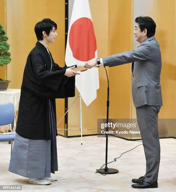 Two-time figure skating Olympic gold medalist Yuzuru Hanyu receives a People's Honor Award certificate from Japanese Prime Minister Shinzo Abe at a...