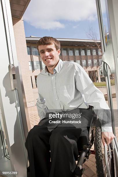 businessman with spinal cord injury in a wheelchair coming in an office door - spinal cord injury stock-fotos und bilder