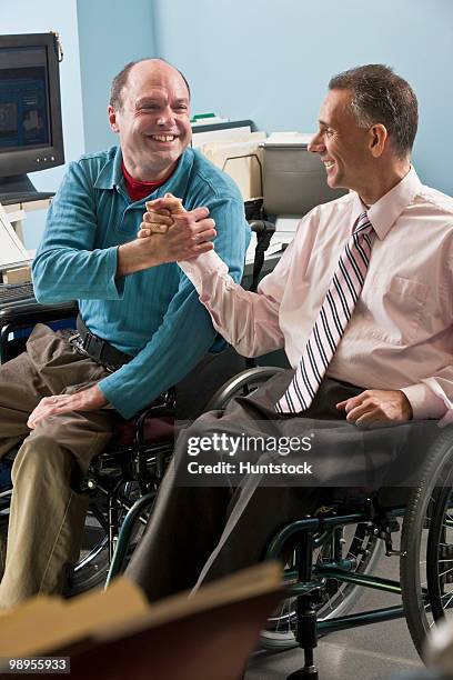 two businessmen shaking hands in an office, one with friedreich's ataxia and another with spinal cord injury - spinal cord injury stock-fotos und bilder