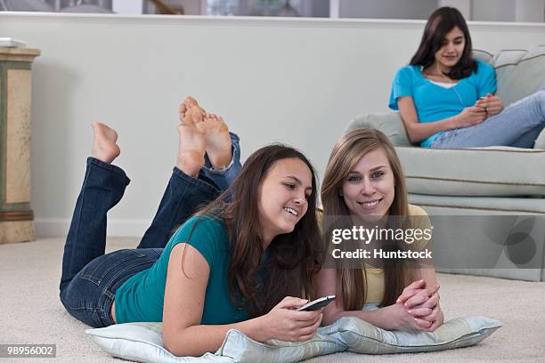 two teenage girls watching television with her friend listening to an mp3 player - girls barefoot in jeans stockfoto's en -beelden