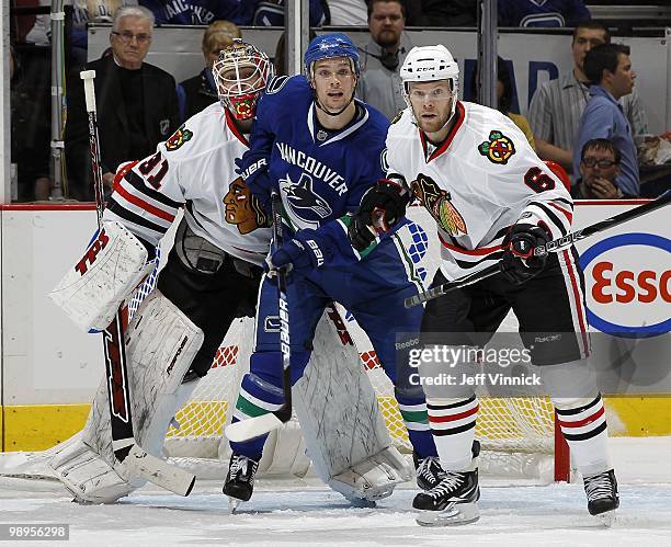 Antti Niemi and teammate Jordan Hendry of the Chicago Blackhawks and Mason Raymond of the Vancouver Canucks watch for a shot from the point in Game...