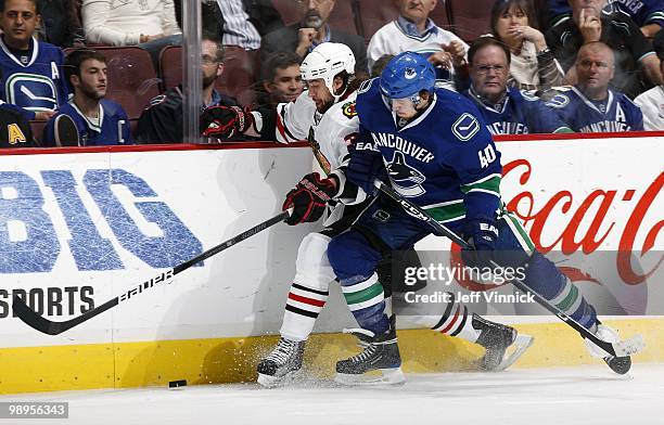 Michael Grabner of the Vancouver Canucks checks Adam Burish of the Chicago Blackhawks into the boards as they battle for the puck in Game Four of the...