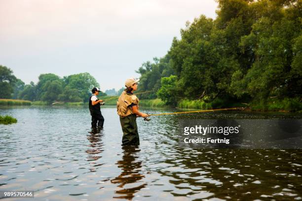 two brothers fishing on a river early on a summer morning - waders imagens e fotografias de stock