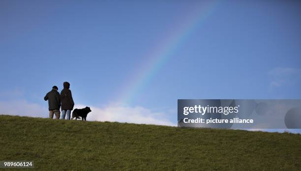 Two strollers with their dog walk along the embankment with a rainbow in the sky in Norddeich, Germany, 02 December 2018. Photo: Mohssen...