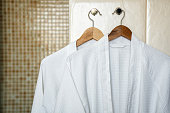 Two white rag bathrobes towels on wooden hangers in the interior of a stylish bathroom. Relax in the hotel for two.