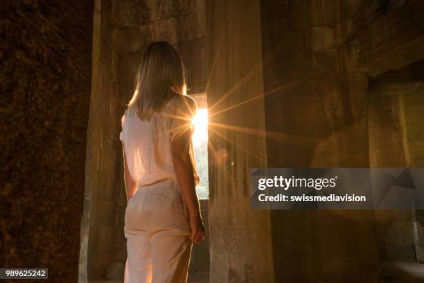 view of tourist traveler exploring ancient temple at sunset, sunbeam passing through window. people travel exploration concept - sun rays through window stock pictures, royalty-free photos & images