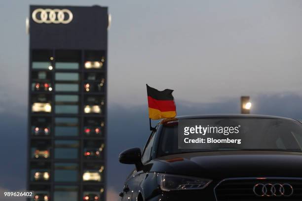 German national flag flies from a used Audi AG automobile as new vehicles sit illuminated in glass display tower at the automaker's showroom at dusk...