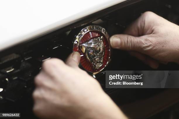 An employee fixes a badge to the front grille of a Jaguar F-type automobile as it moves through the final inspection area at Tata Motors Ltd.'s...