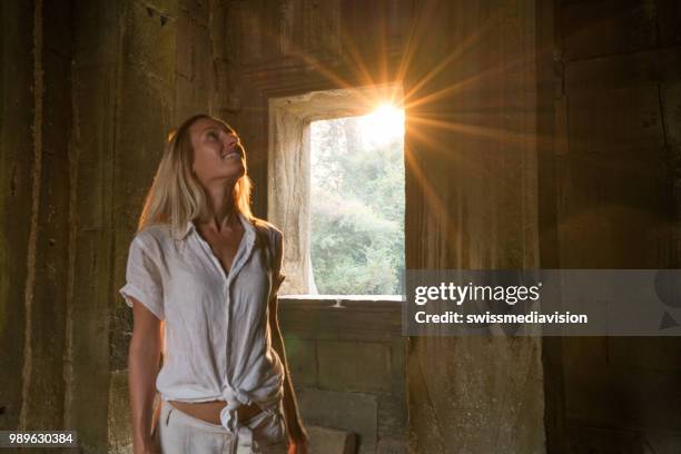 view of tourist traveler exploring ancient temple at sunset, sunbeam passing through window. people travel exploration concept - sun rays through window stock pictures, royalty-free photos & images