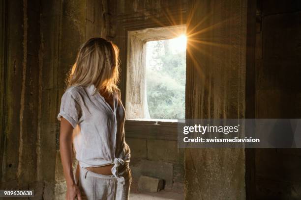 view of tourist traveler exploring ancient temple at sunset, sunbeam passing through window. people travel exploration concept - sun rays through window stock pictures, royalty-free photos & images