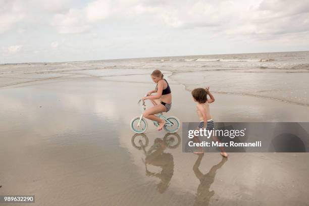 siblings playing on beach riding bike - saint simons island stock-fotos und bilder