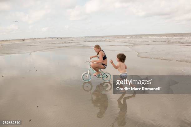 siblings playing on beach riding bike - st simons island stock pictures, royalty-free photos & images