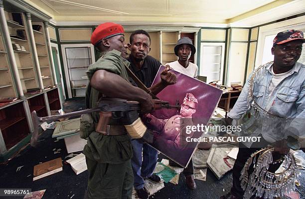 Soldier of the rebel Alliance of Laurent-Desire Kabila, surrounded by looters, uses his weapon to hit a photograph of ousted Zairean President Mobutu...