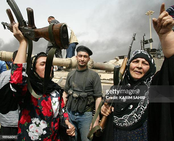 Iraqi women wave Kalashnikovs as they celebrate near a wrecked US Abrams tank south of Baghdad 06 April 2003 which was destroyed in fierce fighting...