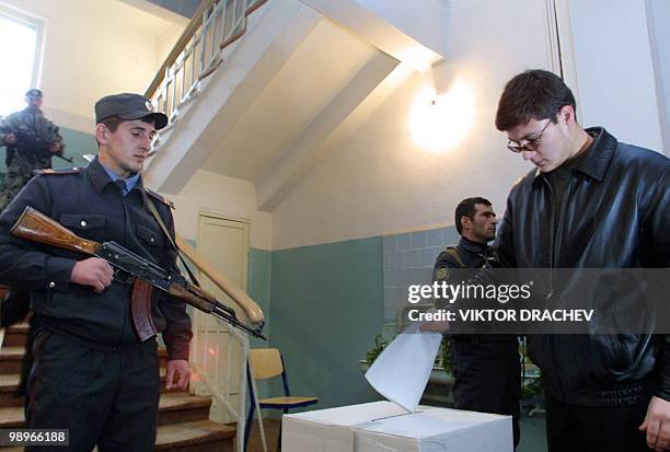 Man casts his ballot next to an armed policemen in a polling station in Grozny, 07 December 2003. Security measures in Chechnya were tightened on...