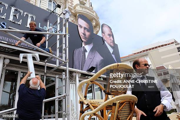 Waiter stands at the Carlton Hotel cafe as workers set up a board promoting the film "Wall Street" a day before the opening of the 63rd edition of...