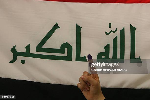 An Iraqi woman shows her ink-stained finger in front of her national flag after casting her vote for the Iraqi general election at a polling station...